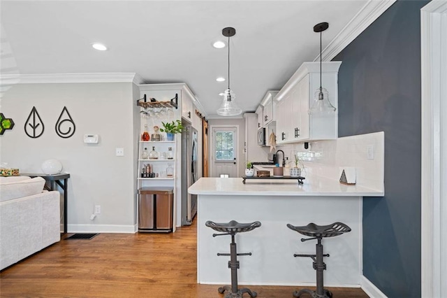 kitchen with pendant lighting, light hardwood / wood-style flooring, ornamental molding, white cabinets, and kitchen peninsula