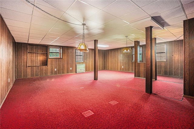 basement with wood walls, a paneled ceiling, and carpet