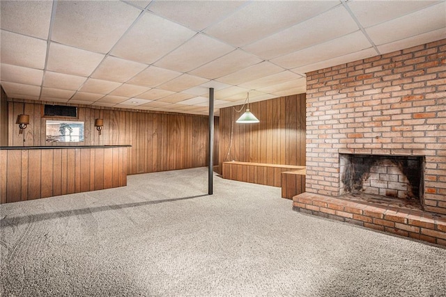 finished below grade area with a drop ceiling, wood walls, a brick fireplace, and carpet