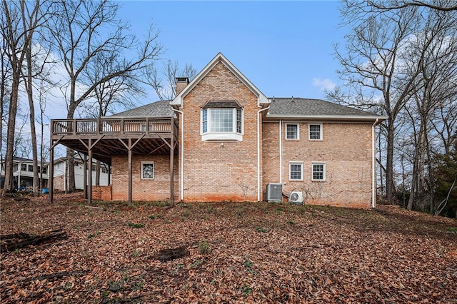 rear view of property featuring brick siding, central air condition unit, a chimney, and a wooden deck