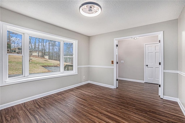 empty room with dark wood finished floors, a textured ceiling, and baseboards