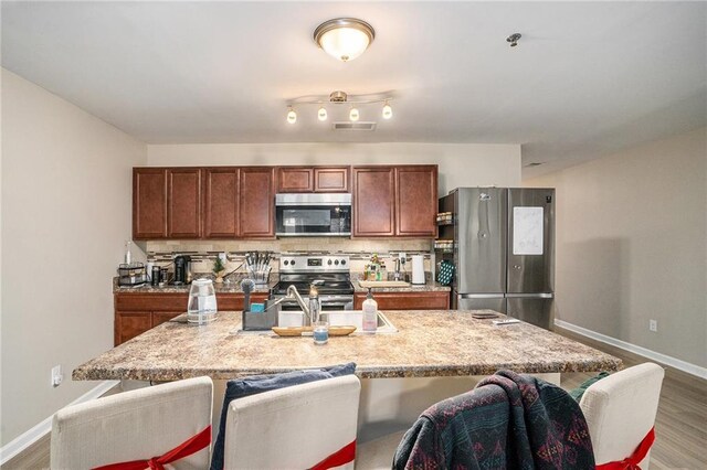 kitchen with a kitchen breakfast bar, decorative backsplash, an island with sink, wood-type flooring, and stainless steel appliances