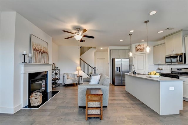 kitchen with a center island with sink, ceiling fan, tasteful backsplash, decorative light fixtures, and stainless steel appliances