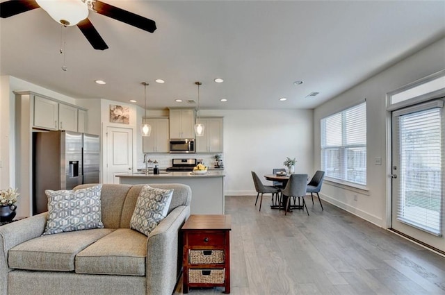 living room featuring light wood-type flooring, ceiling fan, and sink