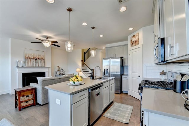 kitchen with decorative backsplash, a center island with sink, hanging light fixtures, and appliances with stainless steel finishes