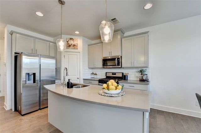 kitchen with hanging light fixtures, stainless steel appliances, tasteful backsplash, gray cabinets, and a center island with sink