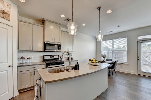 kitchen featuring backsplash, stainless steel appliances, sink, decorative light fixtures, and an island with sink