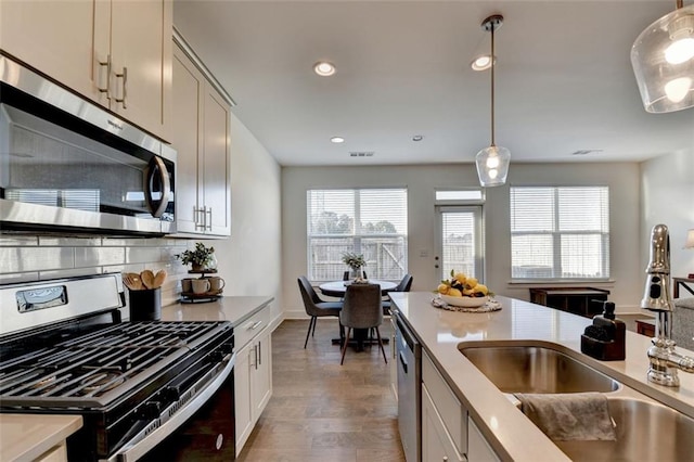 kitchen with sink, hanging light fixtures, tasteful backsplash, appliances with stainless steel finishes, and hardwood / wood-style flooring