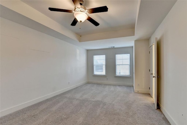 carpeted spare room with a raised ceiling and ceiling fan