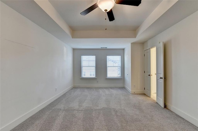 spare room with a tray ceiling, ceiling fan, and light colored carpet