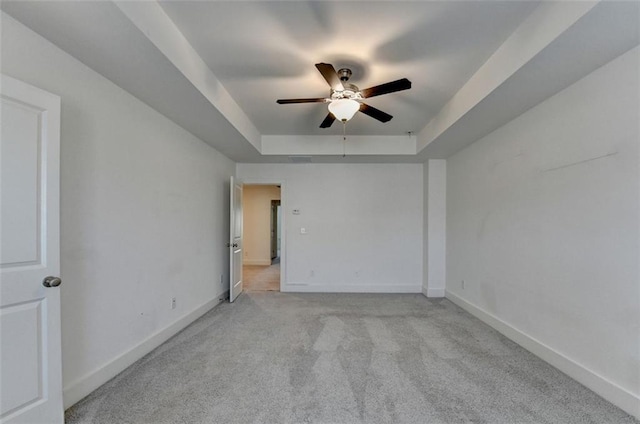 spare room with a tray ceiling, ceiling fan, and light colored carpet