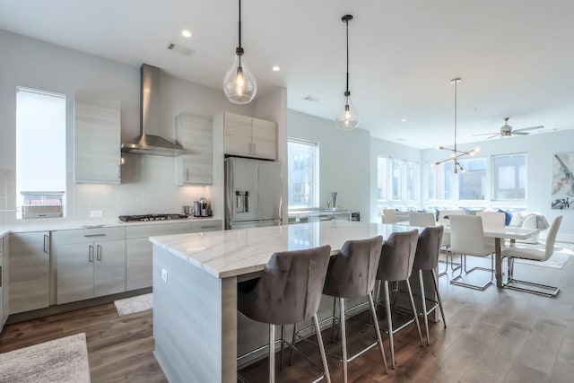 kitchen with decorative light fixtures, a large island, appliances with stainless steel finishes, modern cabinets, and wall chimney exhaust hood