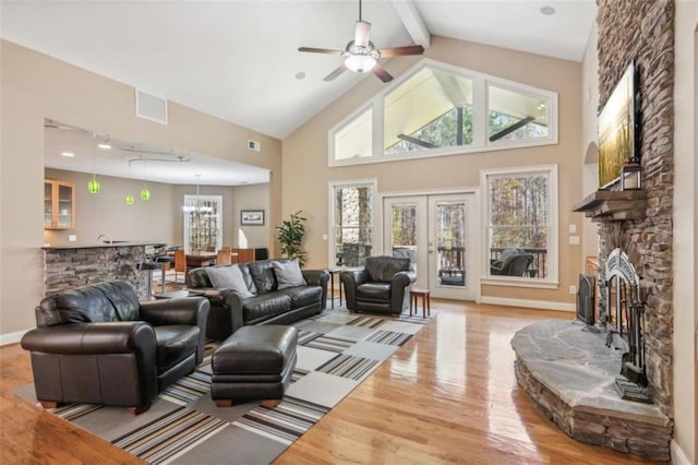 living room with french doors, light wood-type flooring, ceiling fan, beamed ceiling, and a stone fireplace