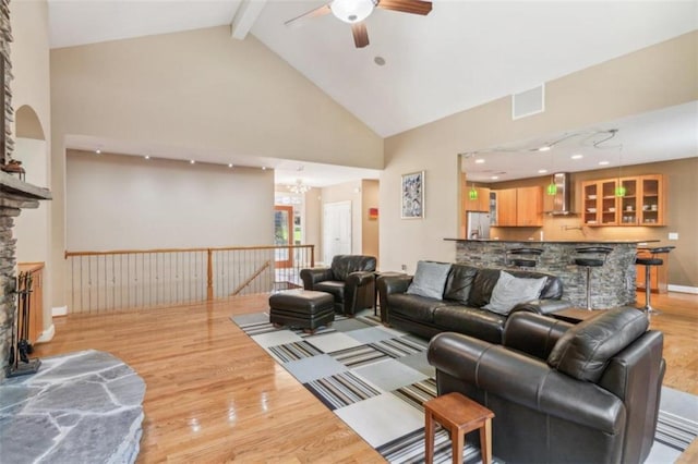 living room with light wood-type flooring, ceiling fan with notable chandelier, beam ceiling, high vaulted ceiling, and a fireplace