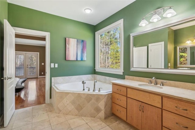 bathroom with vanity, wood-type flooring, tiled tub, and french doors