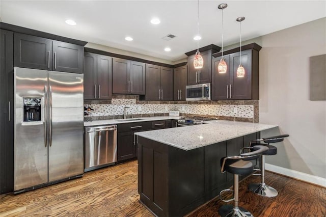 kitchen featuring hanging light fixtures, stainless steel appliances, backsplash, kitchen peninsula, and a kitchen bar