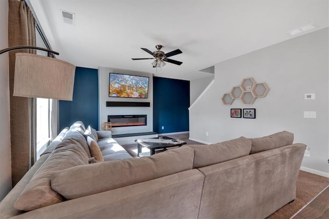 living room with visible vents, baseboards, a glass covered fireplace, and a ceiling fan