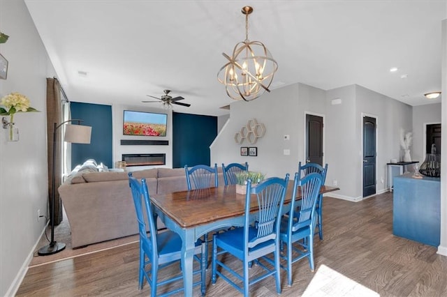 dining space featuring a glass covered fireplace, ceiling fan with notable chandelier, baseboards, and wood finished floors