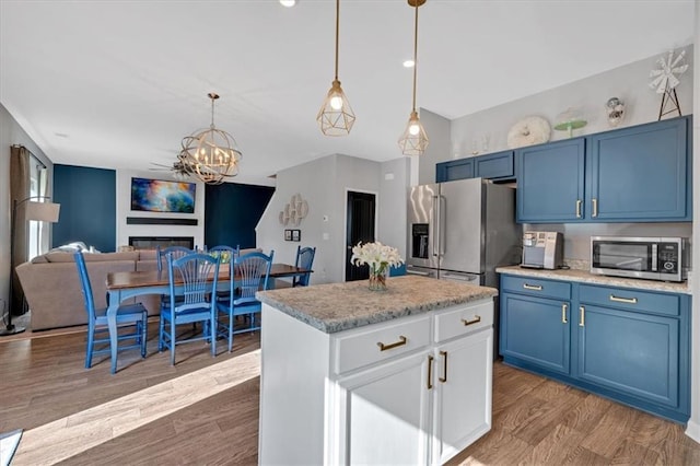 kitchen with wood finished floors, blue cabinetry, stainless steel appliances, a glass covered fireplace, and decorative light fixtures