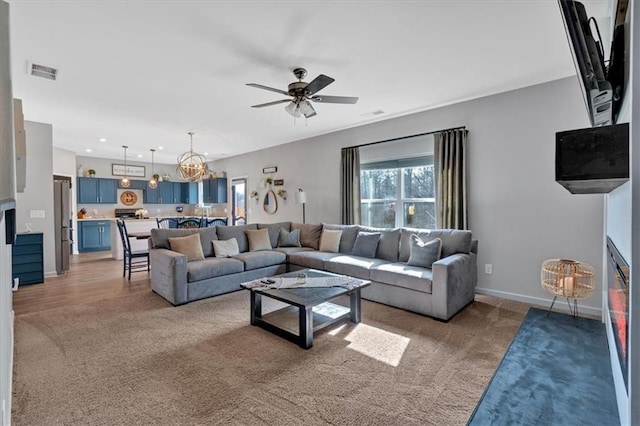 living room with visible vents, ceiling fan with notable chandelier, recessed lighting, baseboards, and light colored carpet