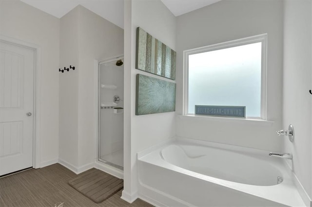 bathroom with wood finished floors, baseboards, a bath, and a shower stall