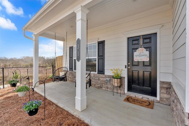 view of exterior entry with a porch, fence, and stone siding