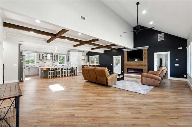 living room featuring high vaulted ceiling, a large fireplace, beamed ceiling, ceiling fan, and light hardwood / wood-style floors