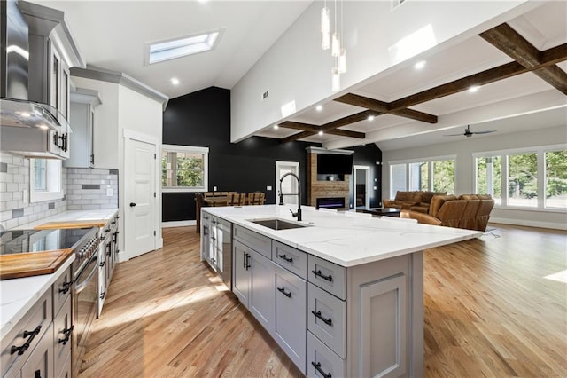 kitchen with sink, gray cabinets, light stone countertops, a kitchen island with sink, and wall chimney range hood