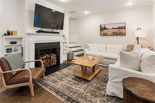 living room featuring wood-type flooring, crown molding, and a tile fireplace