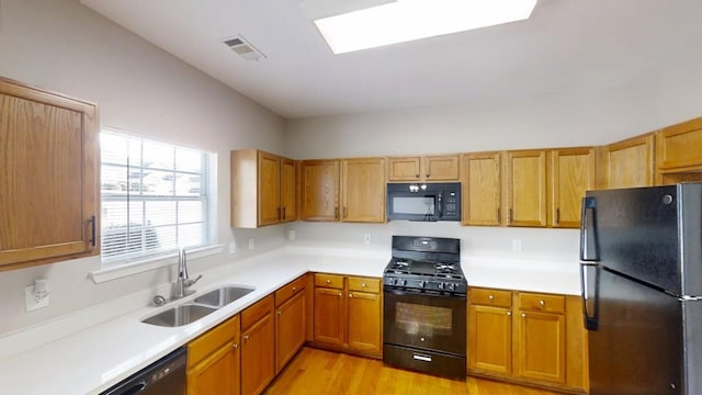 kitchen with light countertops, visible vents, a sink, light wood-type flooring, and black appliances