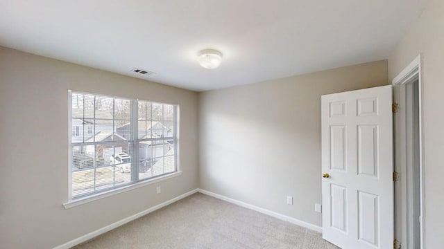 empty room featuring light carpet, visible vents, and baseboards