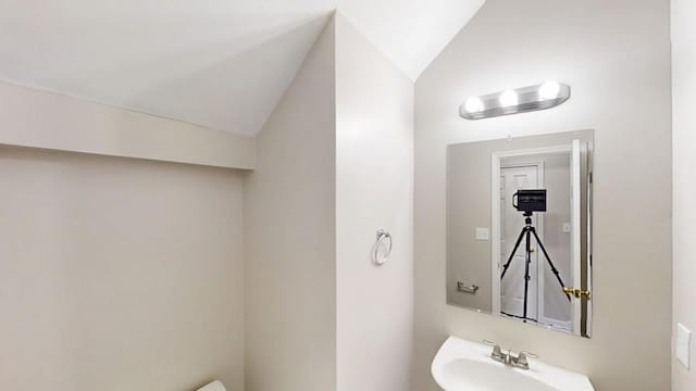 half bathroom with vaulted ceiling and a sink