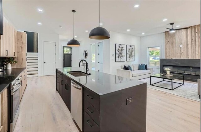 kitchen with appliances with stainless steel finishes, light wood-type flooring, sink, a center island with sink, and decorative light fixtures