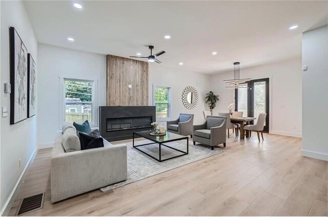 living room with a large fireplace, ceiling fan with notable chandelier, a healthy amount of sunlight, and light hardwood / wood-style flooring