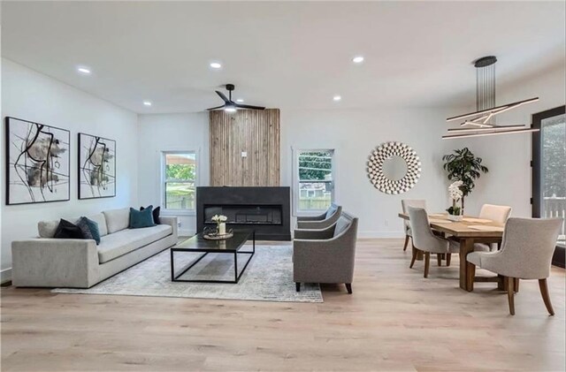 living room featuring ceiling fan, a large fireplace, and light wood-type flooring