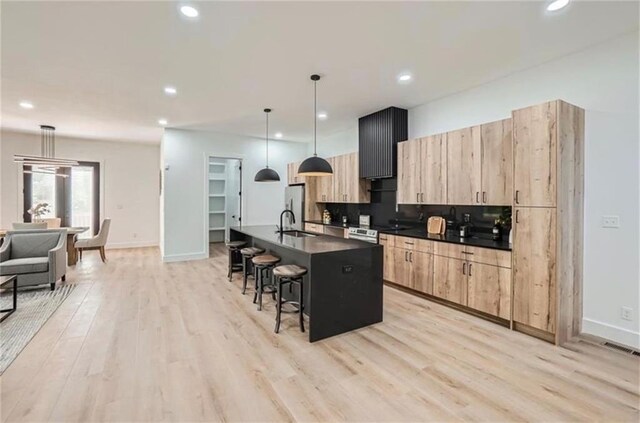 kitchen featuring a kitchen bar, a kitchen island with sink, light brown cabinets, light hardwood / wood-style floors, and hanging light fixtures