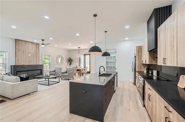 kitchen with sink, light brown cabinets, light hardwood / wood-style flooring, an island with sink, and pendant lighting