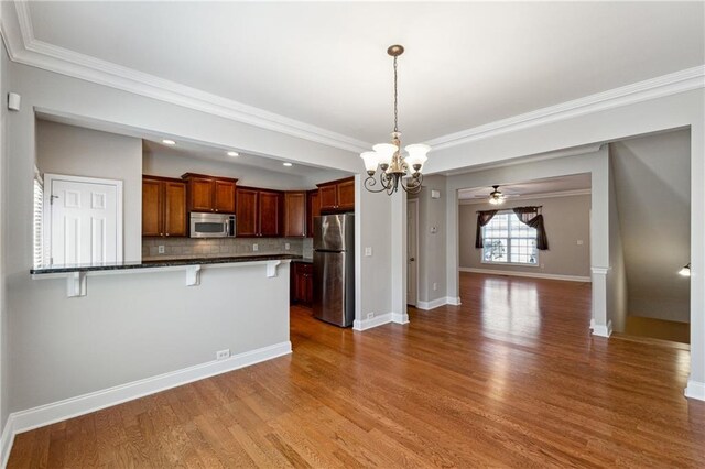 kitchen featuring dark wood-style flooring, a breakfast bar area, stainless steel appliances, decorative backsplash, and baseboards