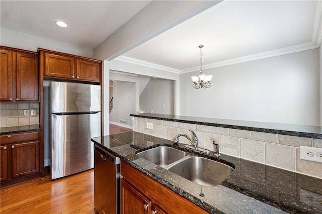 kitchen featuring light wood-style flooring, ornamental molding, stainless steel appliances, pendant lighting, and a sink