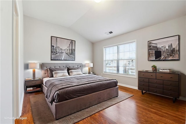 bedroom featuring baseboards, visible vents, vaulted ceiling, and wood finished floors