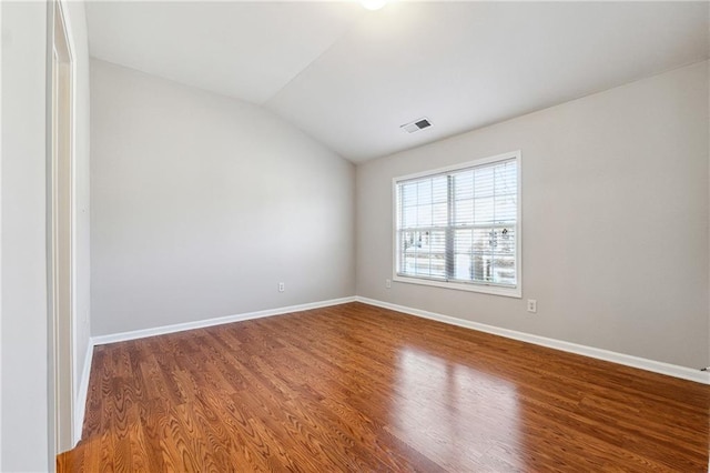 spare room featuring lofted ceiling, visible vents, baseboards, and wood finished floors