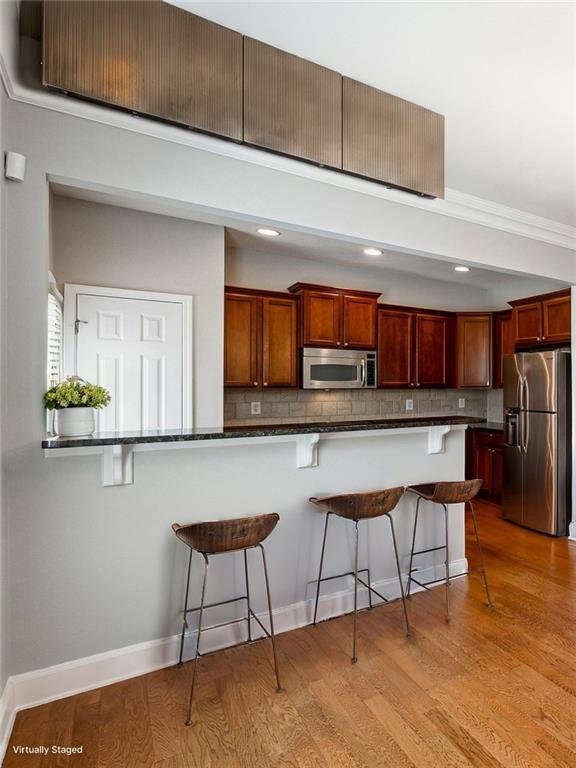 kitchen with appliances with stainless steel finishes, light wood-style flooring, a kitchen breakfast bar, and tasteful backsplash