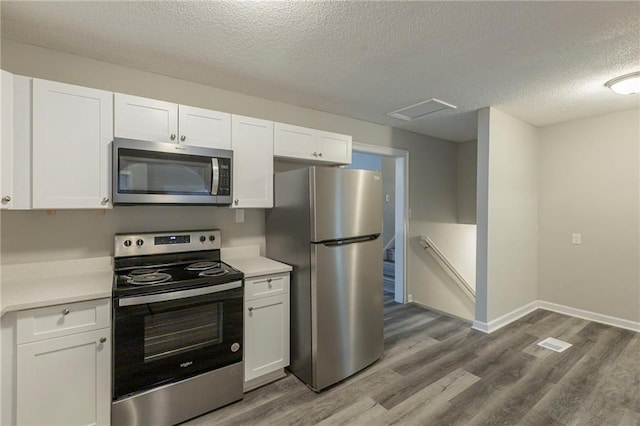 kitchen featuring a textured ceiling, stainless steel appliances, white cabinetry, and hardwood / wood-style flooring