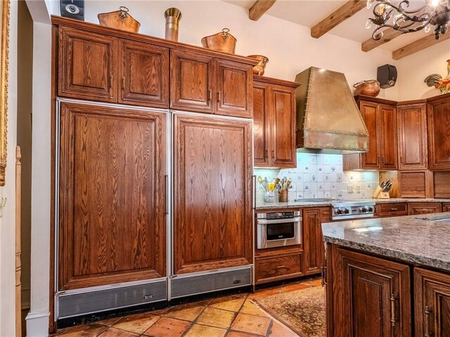 kitchen with beamed ceiling, custom range hood, tasteful backsplash, stainless steel appliances, and dark stone counters