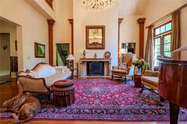 sitting room with hardwood / wood-style floors, high vaulted ceiling, an inviting chandelier, and ornate columns