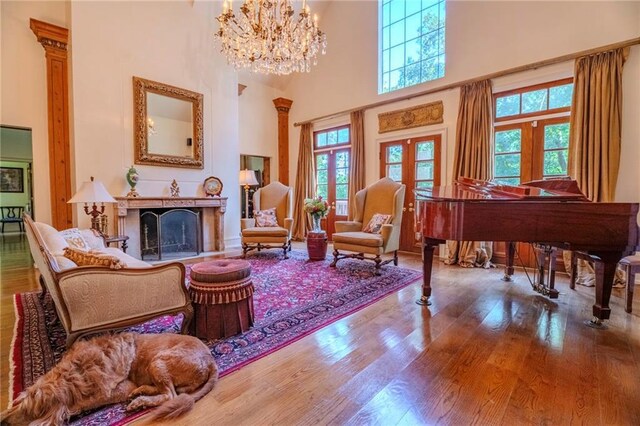 living area featuring a towering ceiling, french doors, hardwood / wood-style floors, and an inviting chandelier