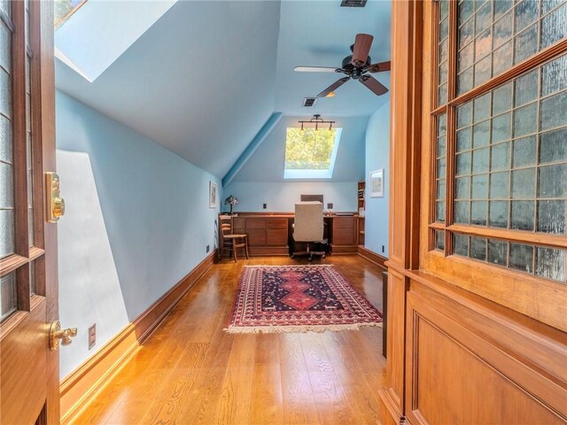 home office featuring light hardwood / wood-style flooring, ceiling fan, and lofted ceiling with skylight