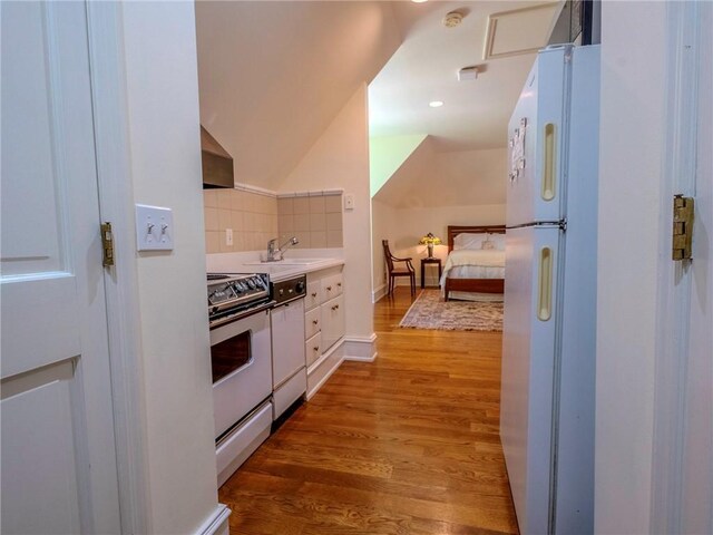 kitchen featuring range hood, backsplash, hardwood / wood-style floors, white appliances, and white cabinetry