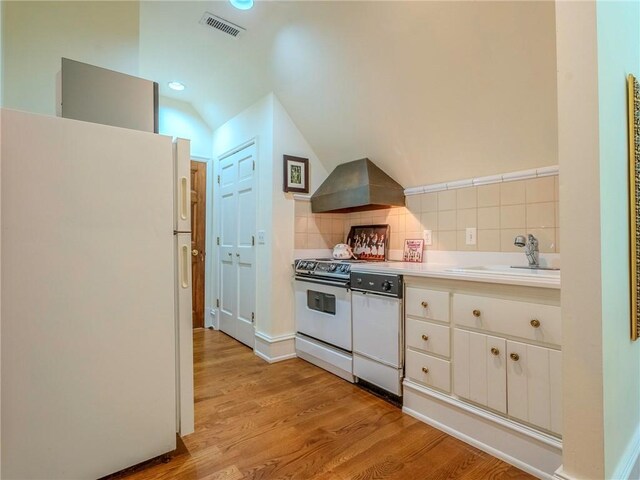 kitchen with vaulted ceiling, white appliances, tasteful backsplash, extractor fan, and white cabinets