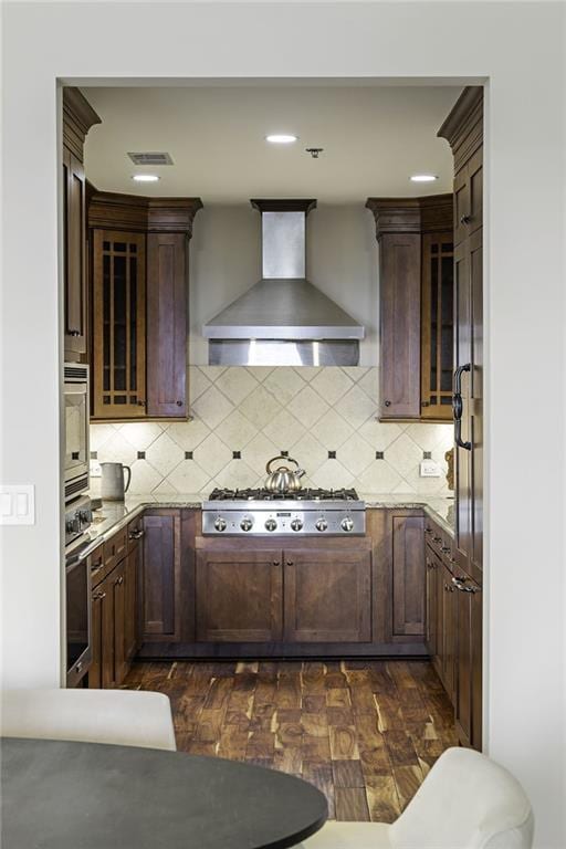 kitchen featuring backsplash, stainless steel appliances, wall chimney exhaust hood, and light stone countertops